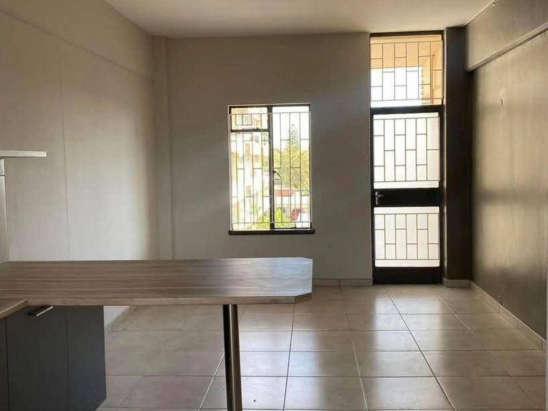 An open-plan living and kitchen area featuring tiled flooring, a breakfast counter, and a secure entrance door with security bars.