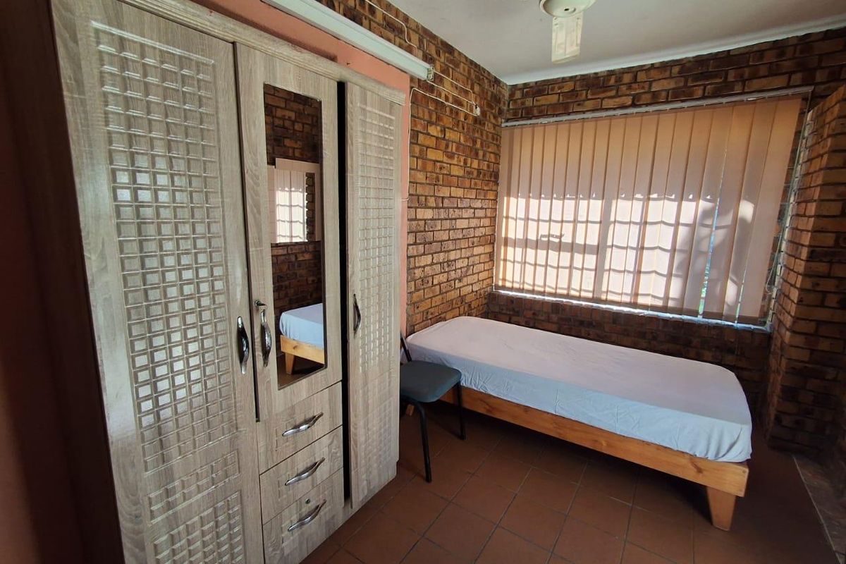 A bedroom featuring exposed brick walls, tiled flooring, and a ceiling fan, offering a rustic aesthetic with functional window blinds.