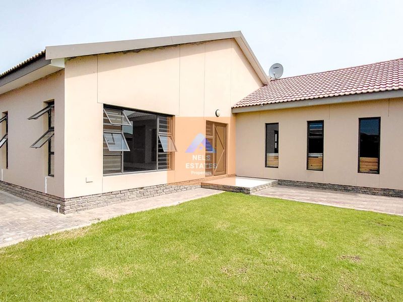 A well-maintained rear exterior view of the house featuring a paved walkway, manicured lawn, and modern tiled roof.