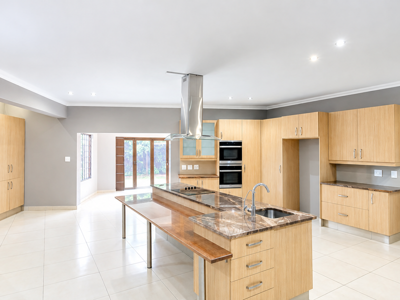 Spacious modern kitchen featuring light wood cabinetry, a large island with stone countertops, integrated double wall oven, and sleek tiled flooring.