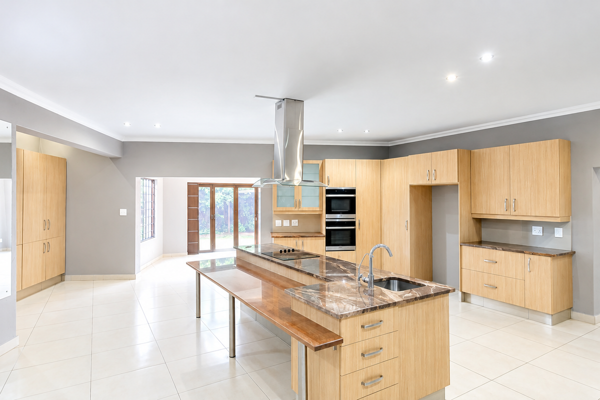 Spacious modern kitchen featuring light wood cabinetry, a large island with stone countertops, integrated double wall oven, and sleek tiled flooring.