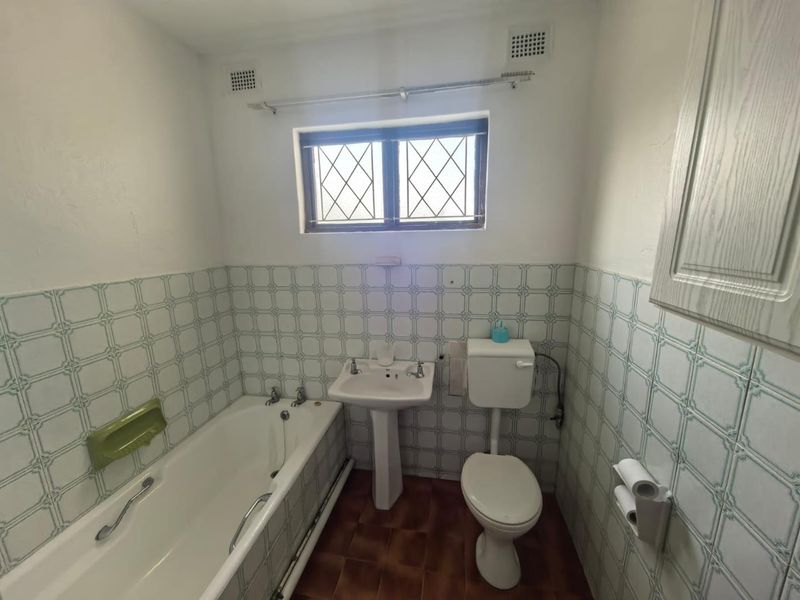 A dated bathroom featuring a pedestal basin, bathtub, and toilet, finished with traditional patterned wall tiles and a leaded glass window.