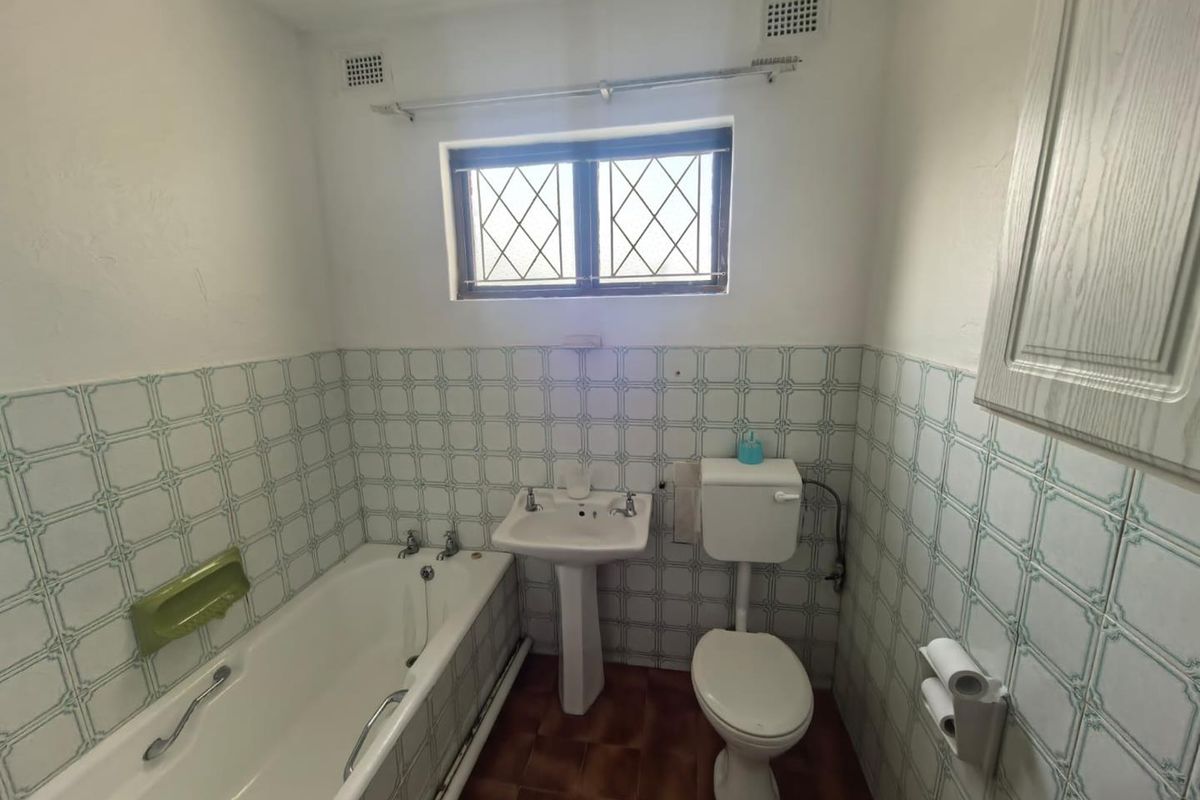 A dated bathroom featuring a pedestal basin, bathtub, and toilet, finished with traditional patterned wall tiles and a leaded glass window.