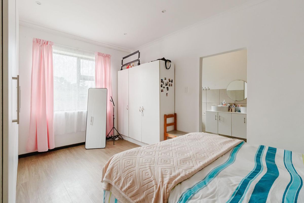 A bright bedroom featuring light wood-look flooring, built-in wardrobes, and an en-suite bathroom with a vanity and mirror.