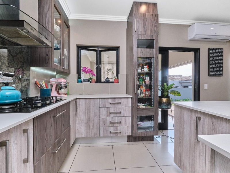 Modern kitchen featuring wood-grain cabinetry, quartz countertops, gas hob, extractor fan, and a built-in pantry, with direct access to the outdoor patio area.