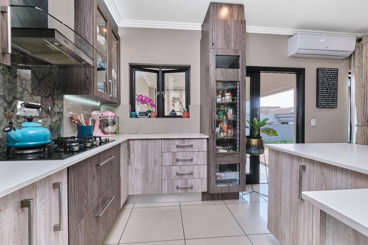 Modern kitchen featuring wood-grain cabinetry, quartz countertops, gas hob, extractor fan, and a built-in pantry, with direct access to the outdoor patio area.