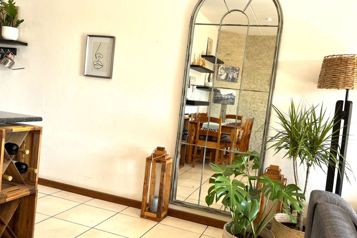A view of a living area featuring tiled flooring and a large arched floor mirror reflecting the adjacent dining space.