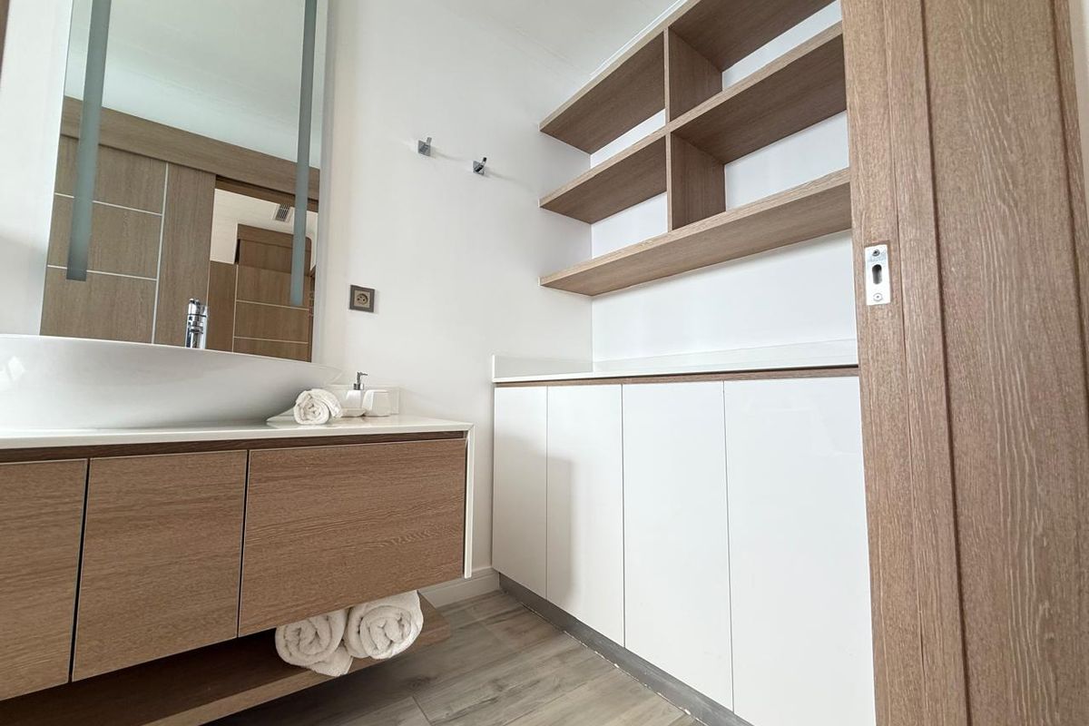 Modern bathroom featuring a floating vanity with integrated basin, illuminated mirror, and extensive built-in cabinetry with open shelving.