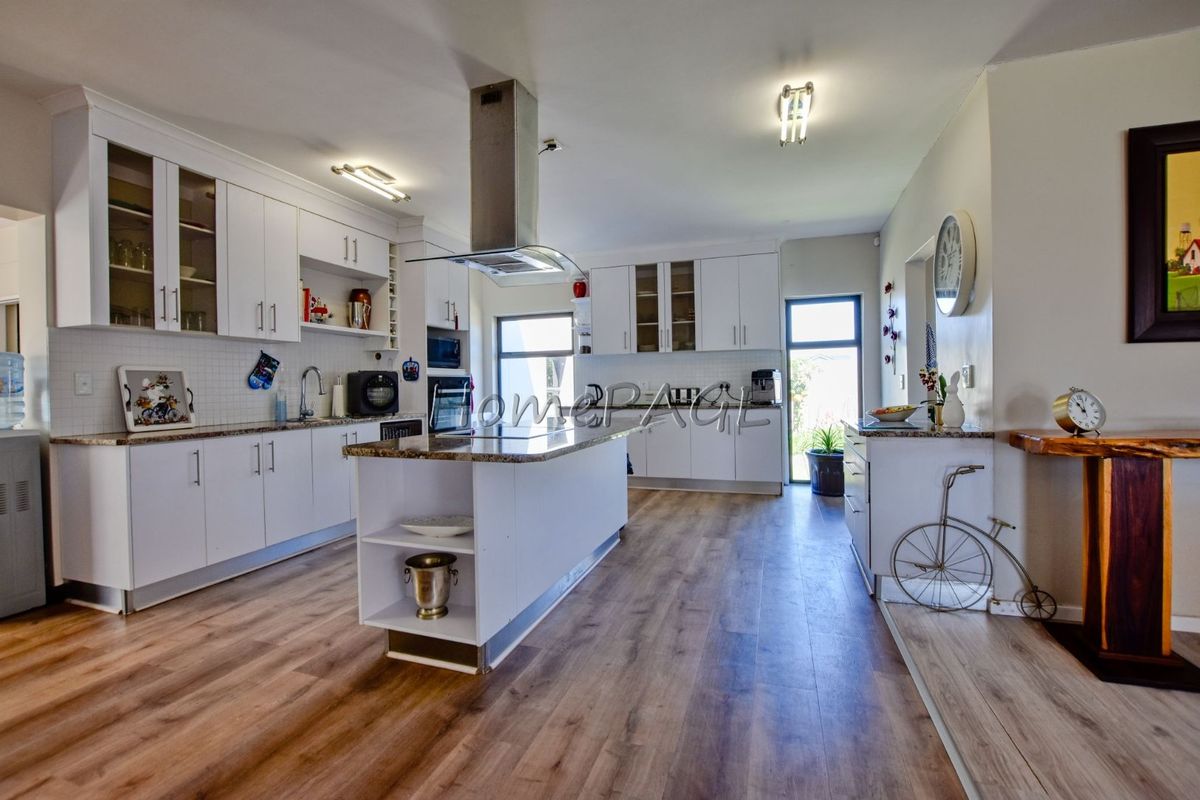 Modern kitchen featuring white cabinetry, granite countertops, a central island with an extractor fan, and durable laminate flooring.