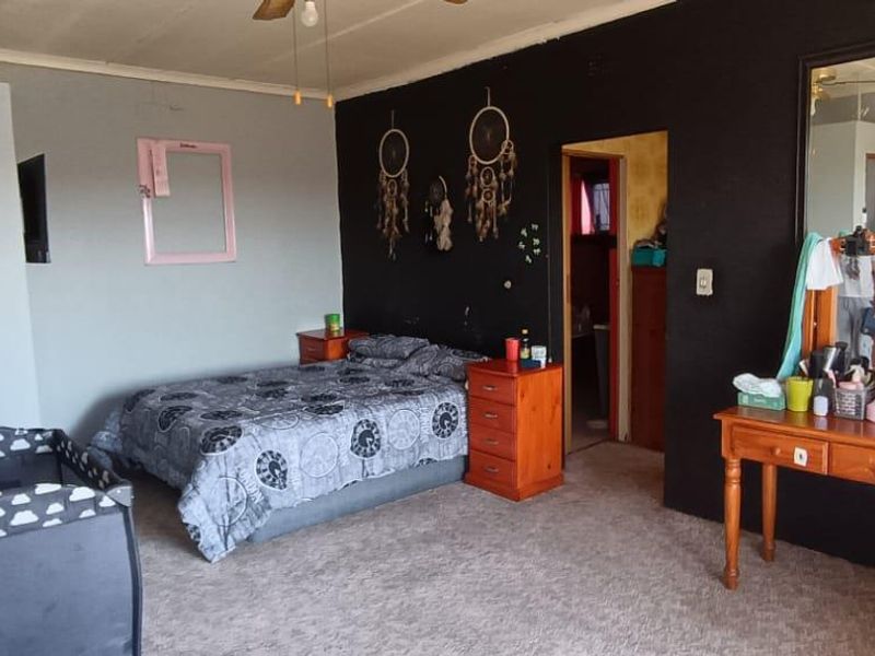 A bedroom featuring carpeted flooring, a ceiling fan, and a large wall-mounted mirror, with dark accent wall paint.