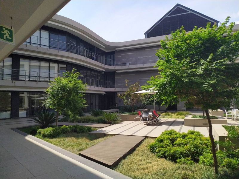 A well-maintained modern office courtyard featuring landscaped gardens, paved walkways, and multi-level building access with contemporary architectural finishes.