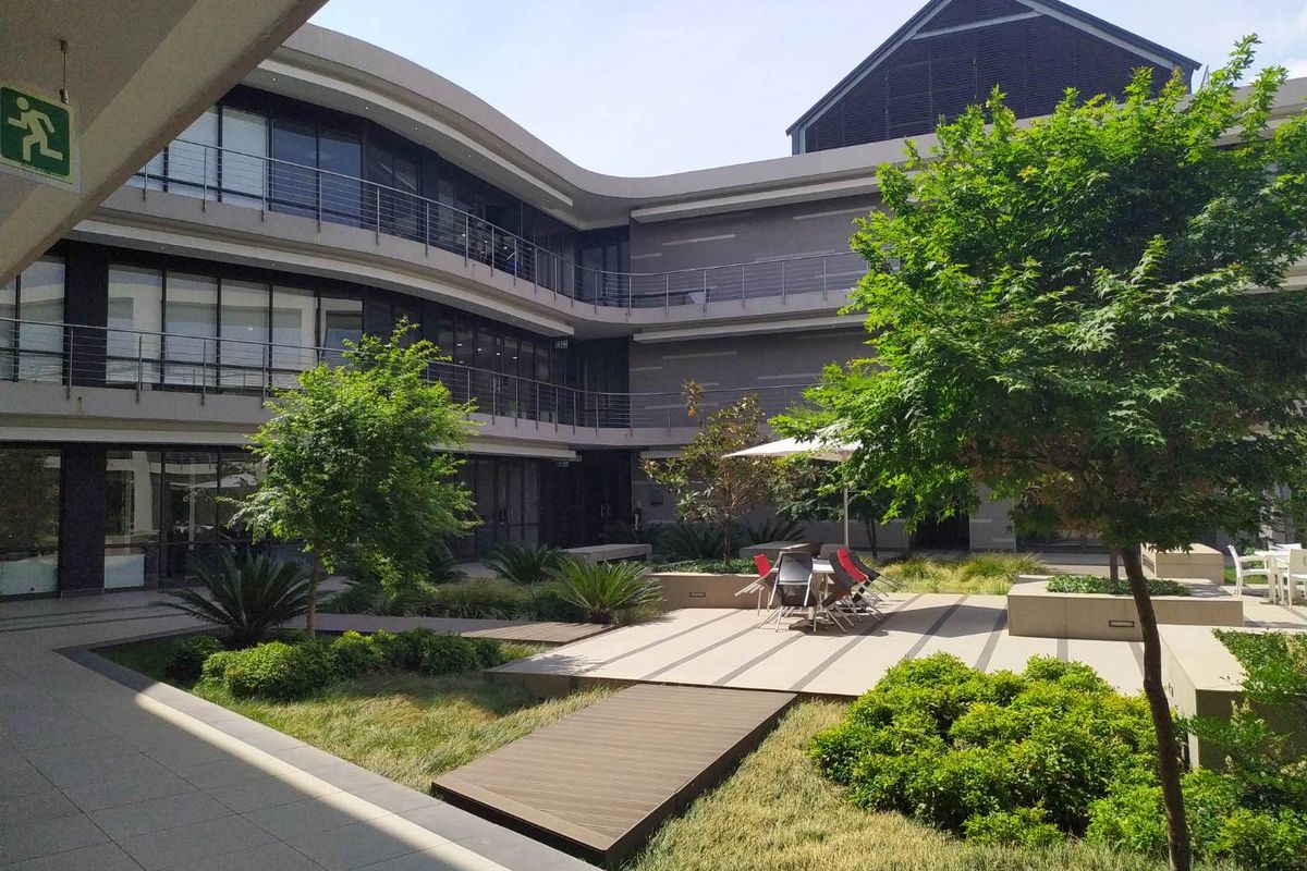 A well-maintained modern office courtyard featuring landscaped gardens, paved walkways, and multi-level building access with contemporary architectural finishes.