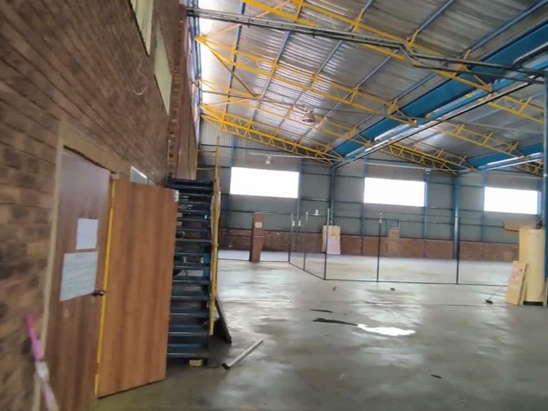 Spacious industrial warehouse interior featuring exposed steel roof trusses, brick walls, concrete flooring, and internal wire mesh partitioning.