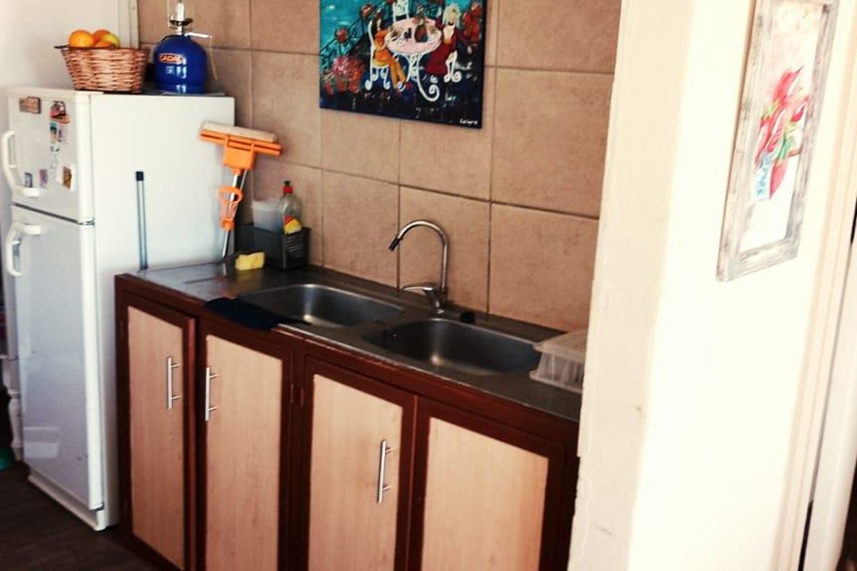 A compact kitchen area featuring a double basin sink, built-in cabinetry, and tiled backsplash.
