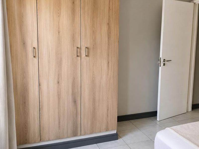 A bedroom featuring light wood-finish built-in wardrobes, neutral wall paint, and clean tiled flooring.