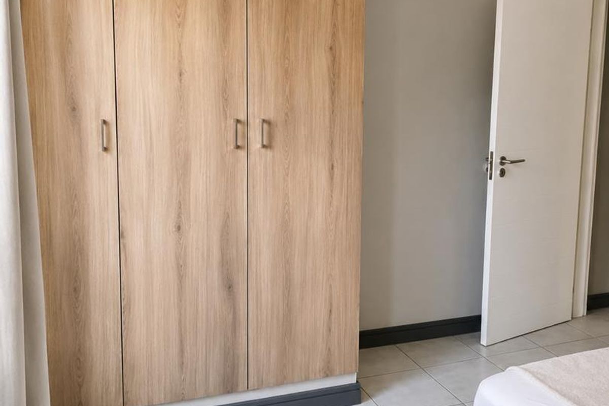 A bedroom featuring light wood-finish built-in wardrobes, neutral wall paint, and clean tiled flooring.