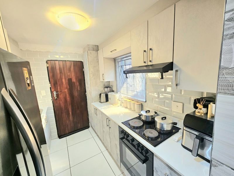A modern, well-maintained kitchen featuring light-toned cabinetry, subway tile backsplash, integrated electric hob and oven, and clean tiled flooring.