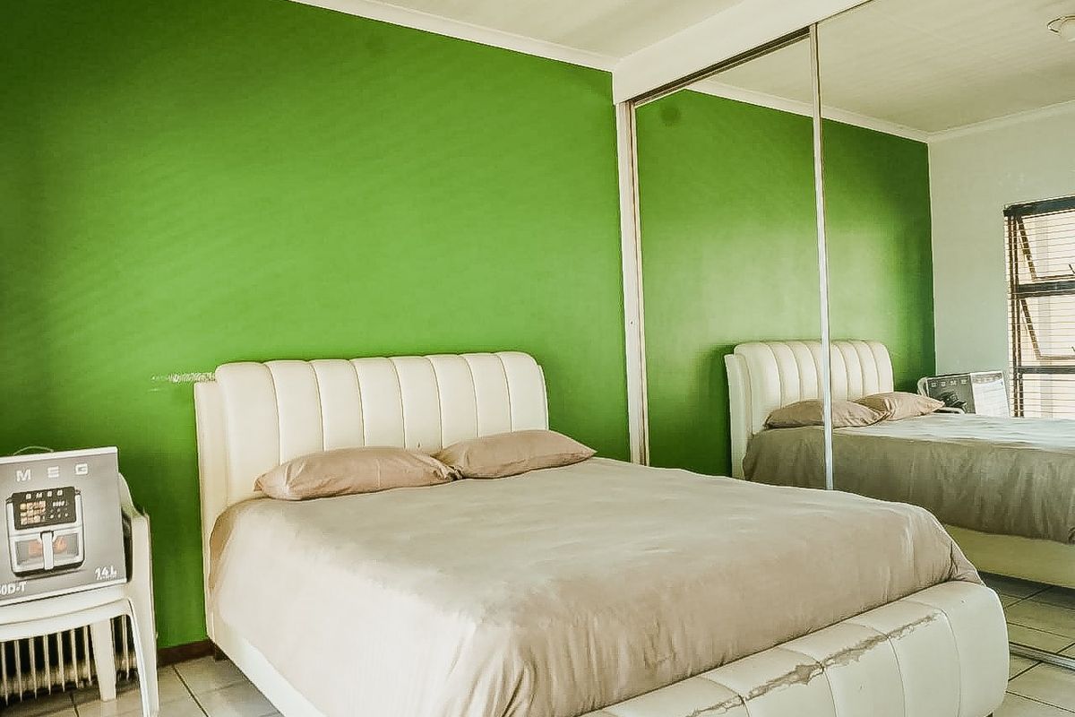 A bedroom featuring tiled flooring, a large built-in mirrored wardrobe, and a window with an aluminium frame.