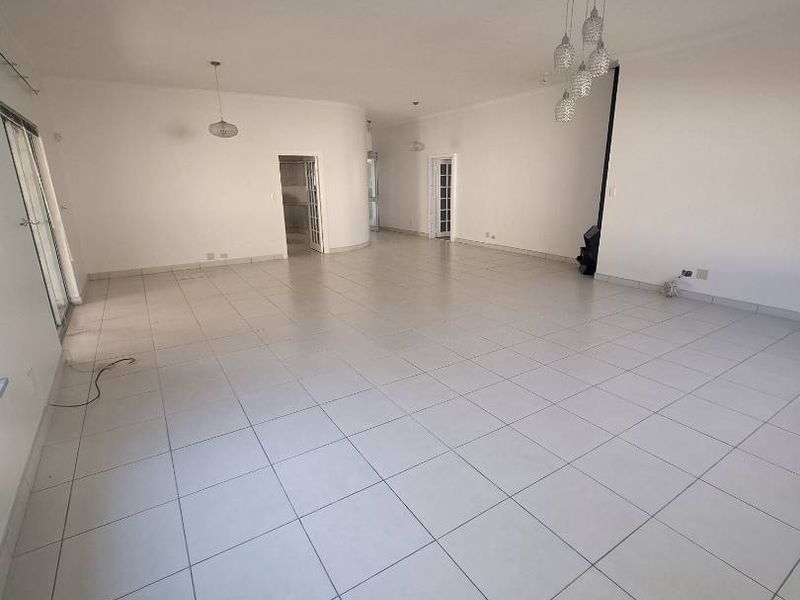A spacious, empty living area featuring neutral tiled flooring, modern pendant lighting, and large sliding glass doors providing access to the exterior.