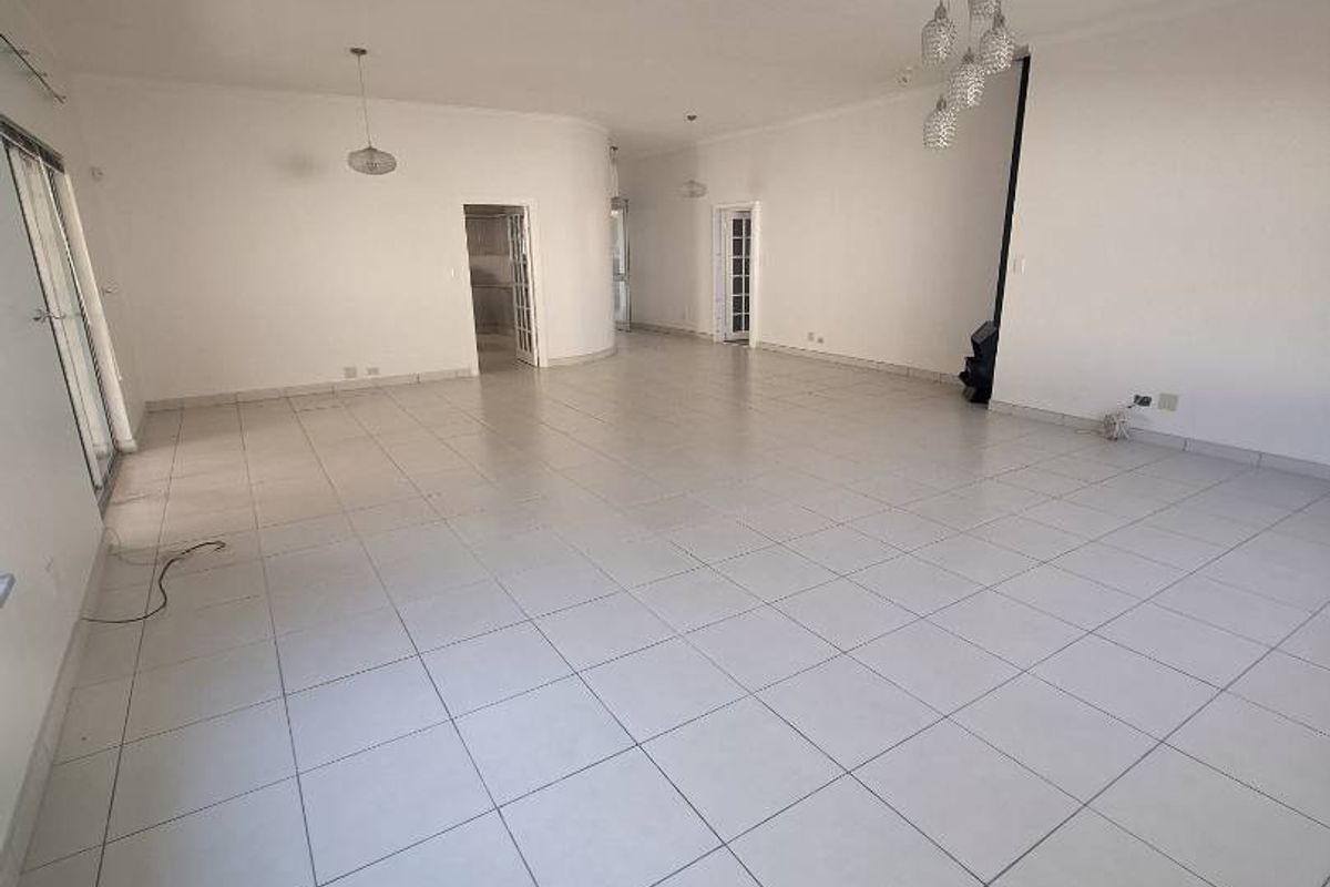 A spacious, empty living area featuring neutral tiled flooring, modern pendant lighting, and large sliding glass doors providing access to the exterior.