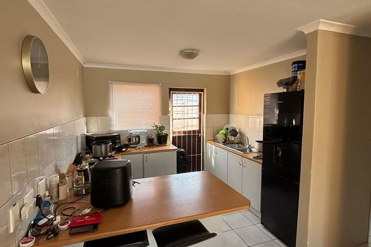 Functional kitchen featuring a breakfast bar, tiled splashbacks, and direct access to the exterior through a security door.