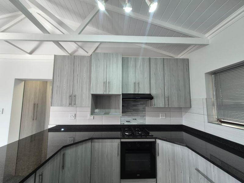 Modern kitchen featuring light wood-grain cabinetry, black granite countertops, built-in gas hob, oven, and an attractive exposed beam ceiling.
