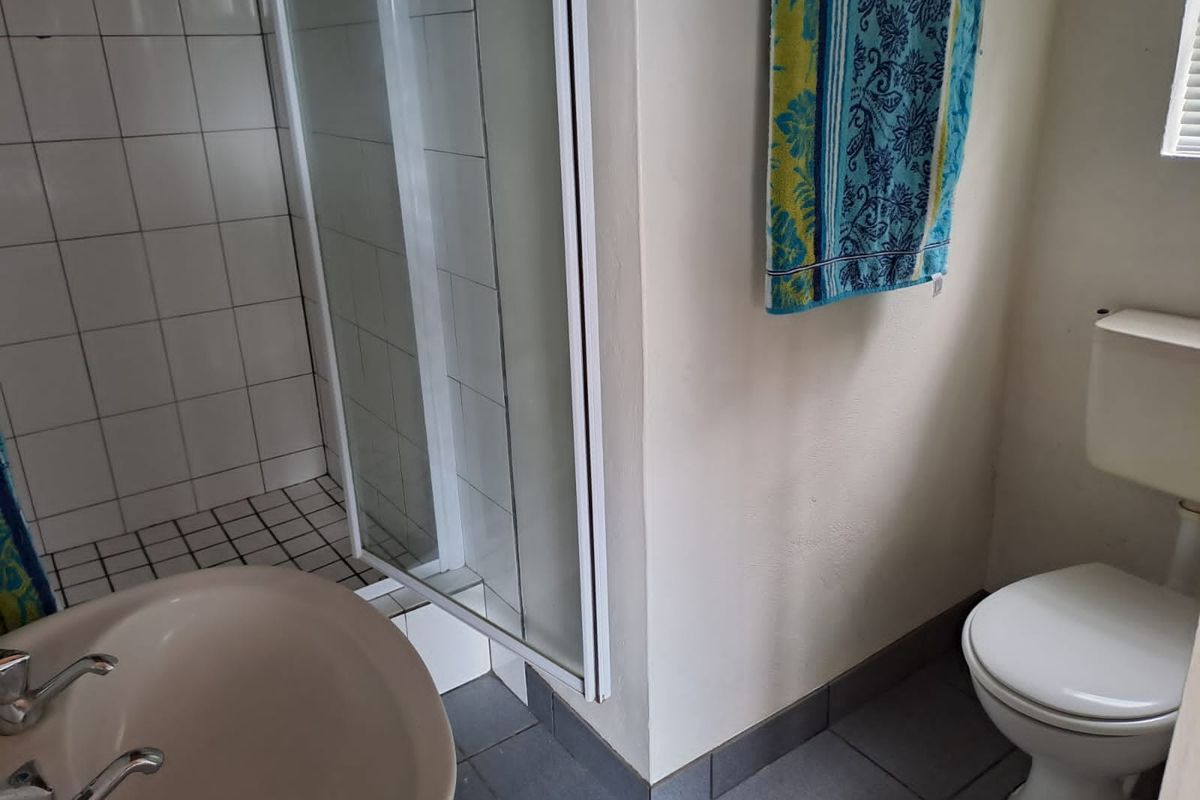 A functional bathroom featuring a shower enclosure, pedestal basin, and toilet with tiled flooring and wall finishes.