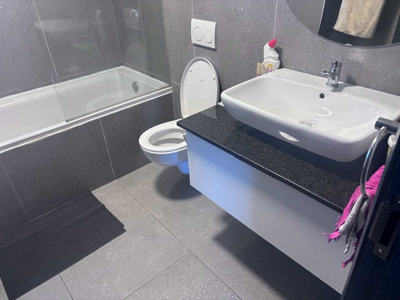 Modern bathroom featuring a floating vanity with granite countertop, vessel sink, wall-mounted toilet, and a built-in bathtub with a glass shower screen.