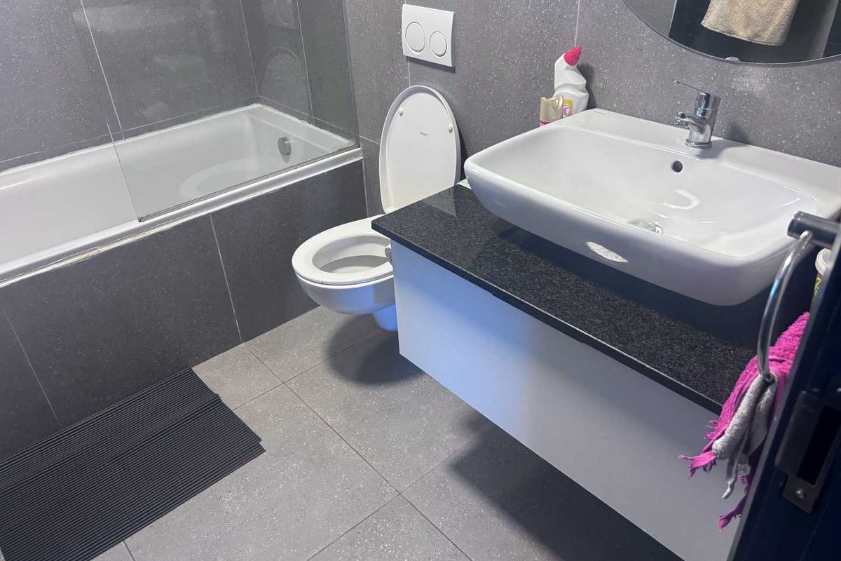 Modern bathroom featuring a floating vanity with granite countertop, vessel sink, wall-mounted toilet, and a built-in bathtub with a glass shower screen.