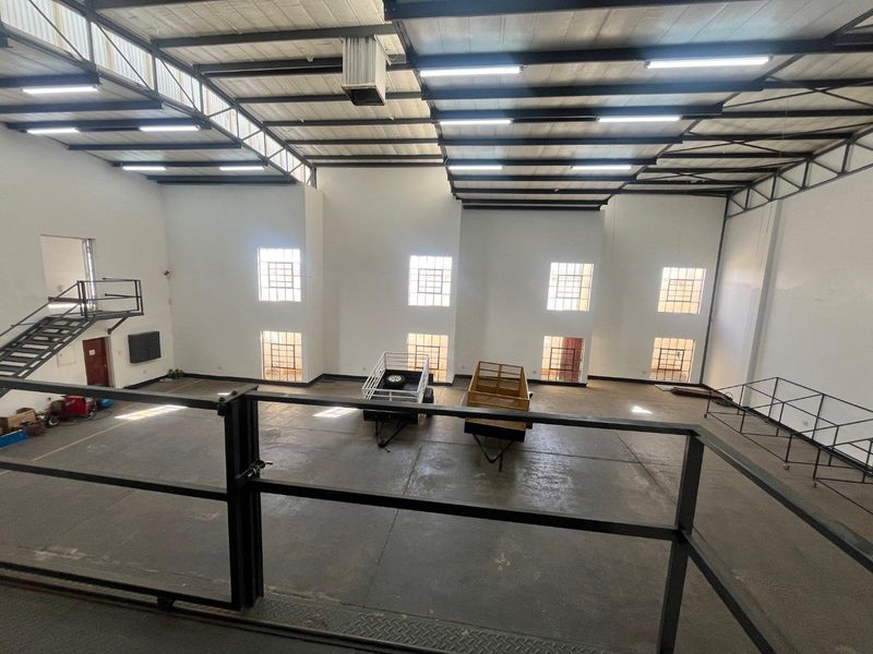 Spacious industrial utility area featuring high ceilings, concrete flooring, mezzanine level access, and ample natural light through large industrial windows.
