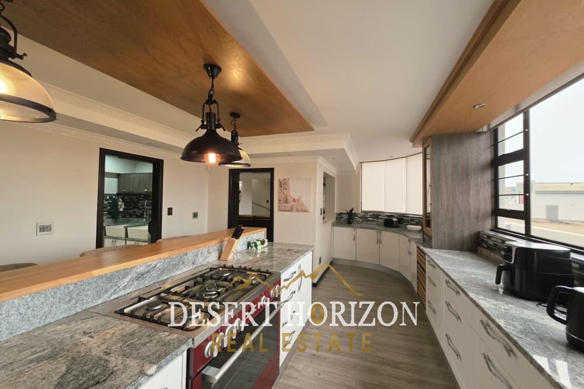 Modern kitchen featuring granite countertops, a central island with a gas hob, built-in oven, and stylish wooden bulkhead ceiling details.