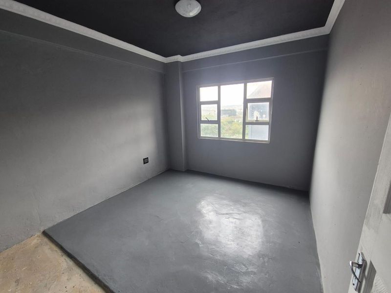 An empty bedroom featuring grey painted walls, a dark ceiling, and a multi-pane window, providing a blank canvas for interior design.