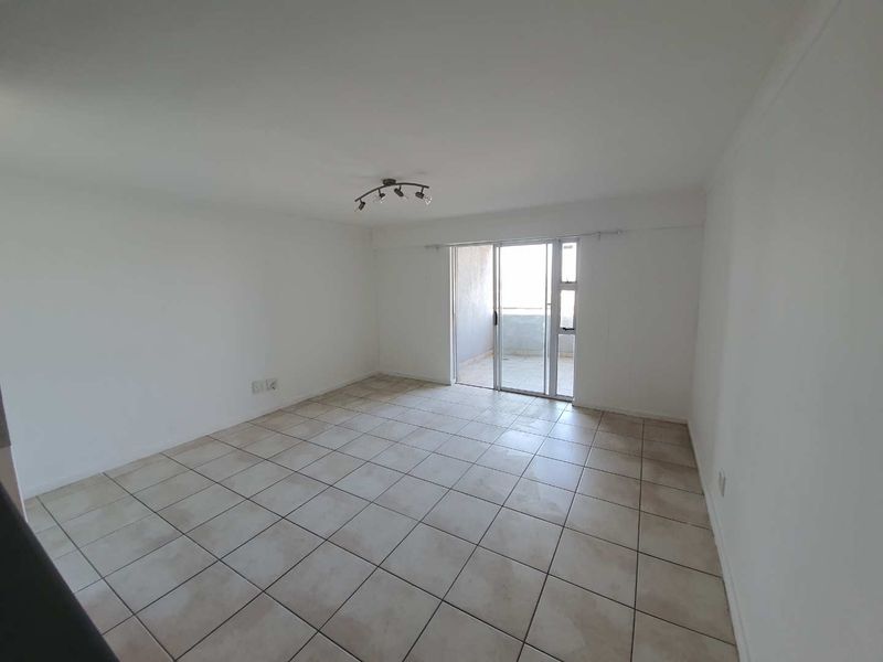A spacious, empty living area featuring neutral tiled flooring and a sliding glass door providing access to an outdoor balcony.