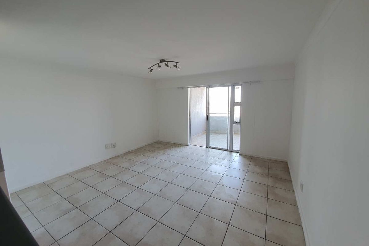 A spacious, empty living area featuring neutral tiled flooring and a sliding glass door providing access to an outdoor balcony.