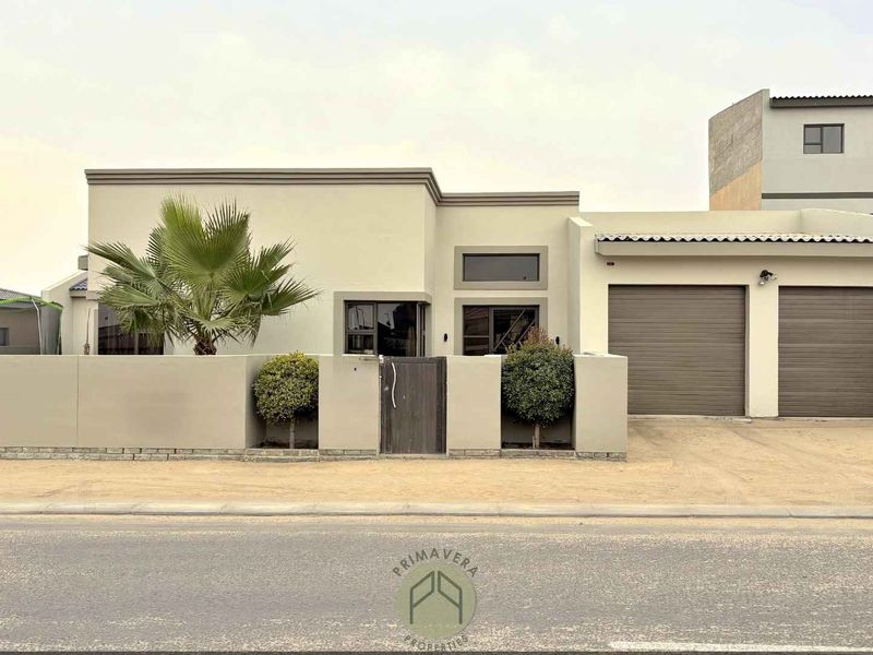 Modern single-story residential property featuring a double garage with roller shutter doors, a secure boundary wall, and a private pedestrian entrance.