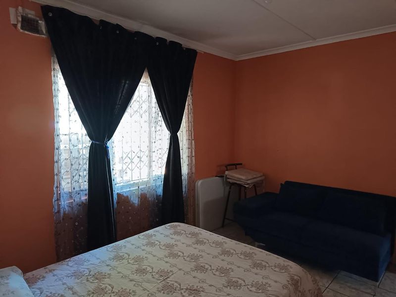 A bedroom featuring tiled flooring, a window with a security gate, and orange painted walls.