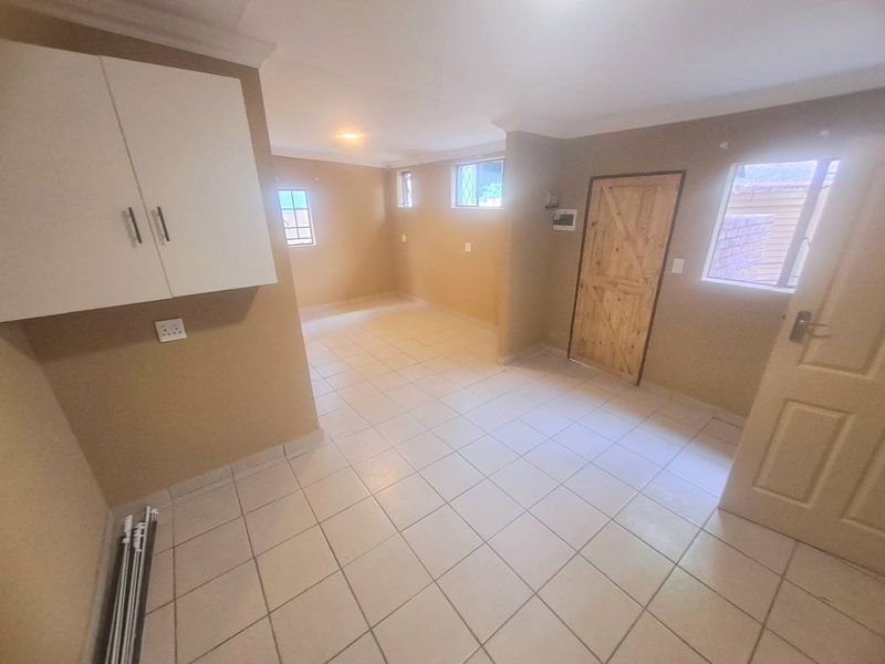 An empty kitchen area featuring tiled flooring, wall-mounted cabinetry, and a timber door, offering a blank canvas for potential renovation.