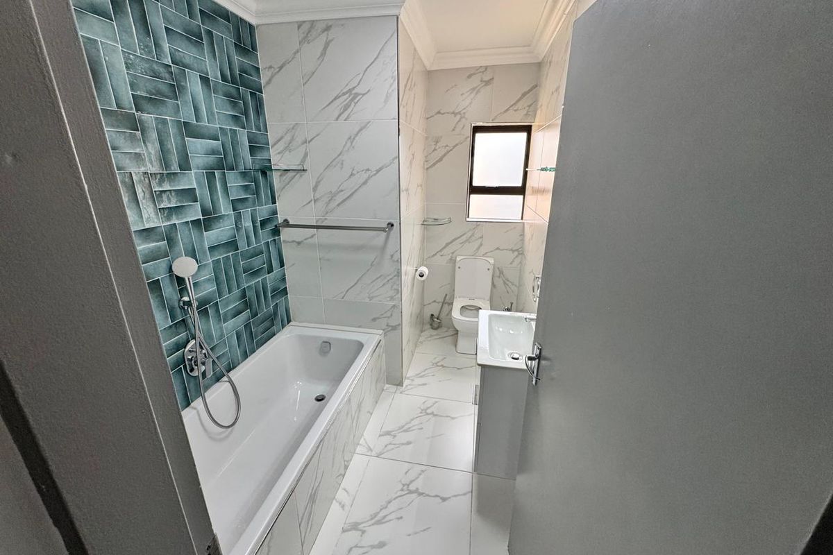 Modern bathroom featuring a built-in bathtub with decorative teal tiling, marble-look floor and wall tiles, a pedestal basin, and a toilet.
