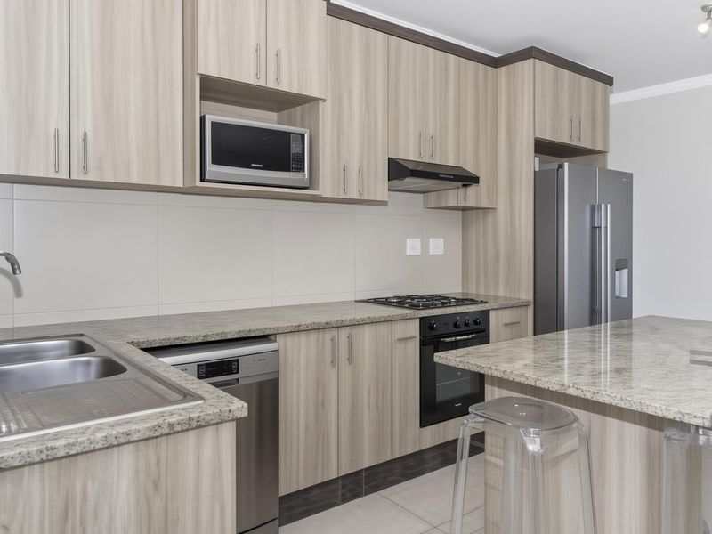 Modern kitchen featuring light wood-grain cabinetry, granite countertops, a central island, and integrated stainless steel appliances including a gas hob and oven.