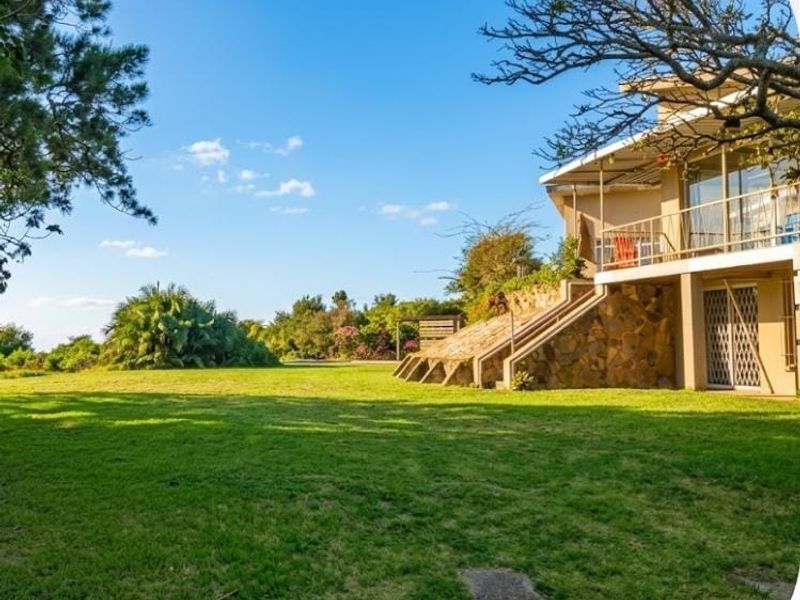 Rear view of the property featuring a spacious lawn, stone-clad foundation, and an elevated balcony with metal railings.