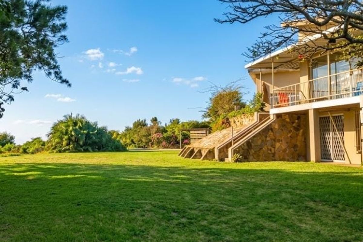 Rear view of the property featuring a spacious lawn, stone-clad foundation, and an elevated balcony with metal railings.