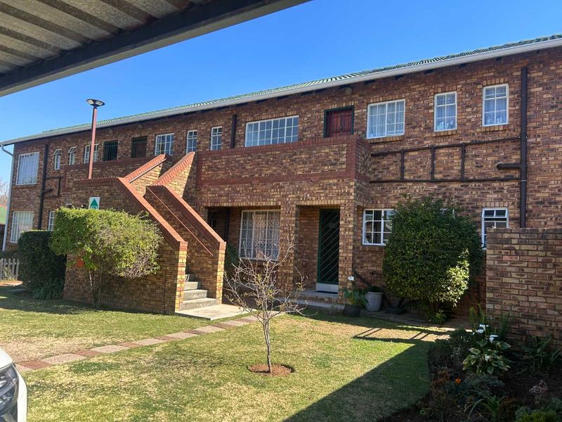Rear view of a multi-story townhouse complex featuring face brick construction, external staircases, and established garden areas.