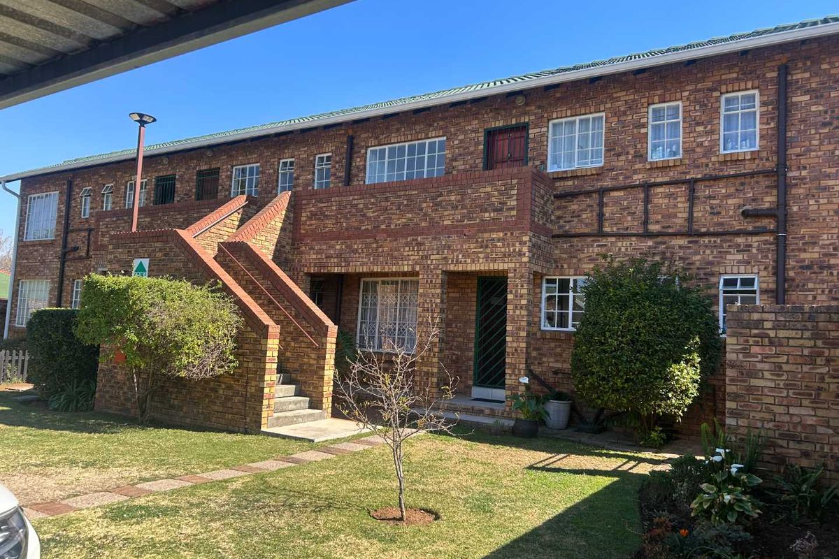 Rear view of a multi-story townhouse complex featuring face brick construction, external staircases, and established garden areas.