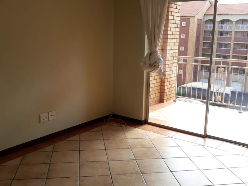 An empty living room featuring tiled flooring and a large sliding glass door that opens onto a private balcony.