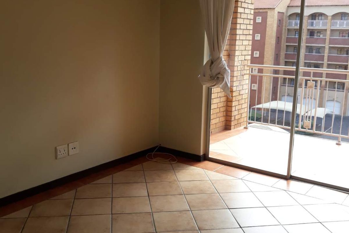 An empty living room featuring tiled flooring and a large sliding glass door that opens onto a private balcony.