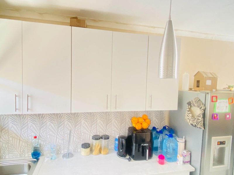 A kitchen area featuring white cabinetry, a patterned tile backsplash, and a stainless steel pendant light, showing signs of wear near the ceiling.