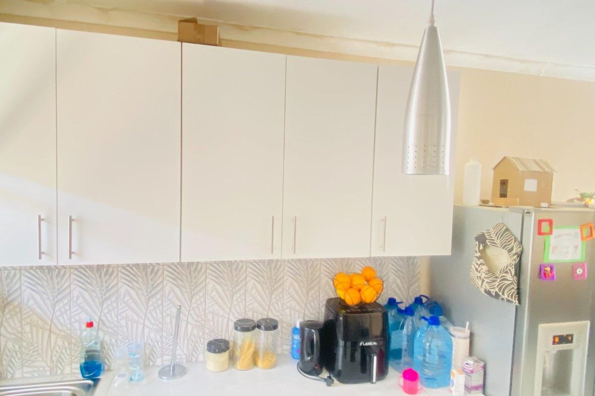 A kitchen area featuring white cabinetry, a patterned tile backsplash, and a stainless steel pendant light, showing signs of wear near the ceiling.