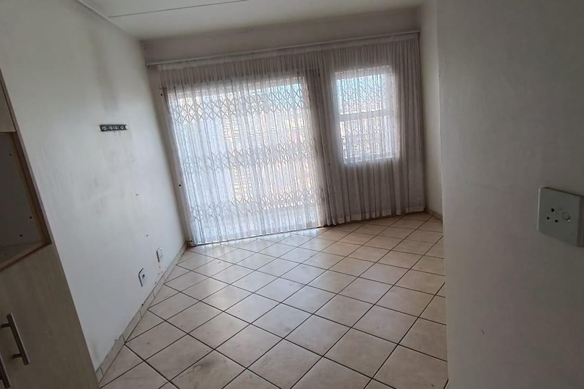 An empty living area featuring tiled flooring, built-in cabinetry, and a sliding glass door with a security gate leading to the exterior.