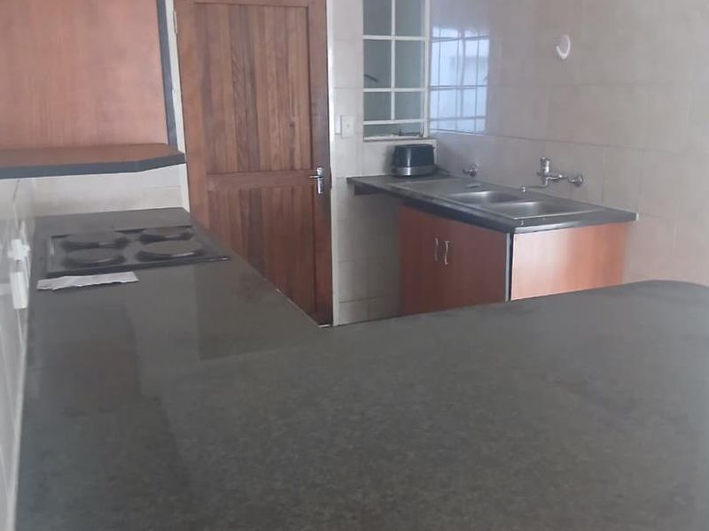A functional kitchen featuring granite countertops, built-in hob, double sink, and wooden cabinetry with tiled splashbacks.