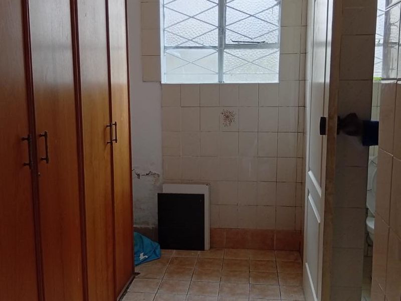 A functional hallway featuring built-in wooden cabinetry, ceramic tiled flooring, and a leaded glass window, requiring some cosmetic maintenance and updates.
